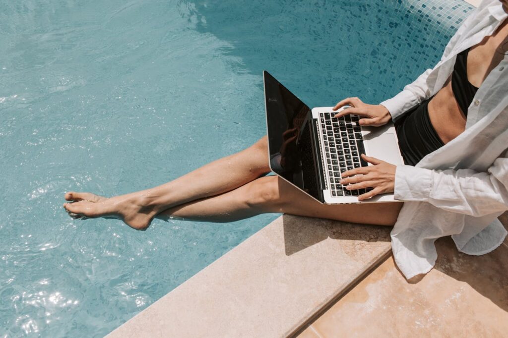 pexels-photo-7903142 A woman in swimwear working on a laptop by the pool, showcasing summer remote work lifestyle.